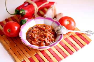 Hot chilli pepper tomato sauce paste with garlic in bowl closeup. Adjika, hot harissa sauce - spicy hot paste of chilli pepper, tomato on table. Tomato hot ketchup sauce with chilli pepper paste food