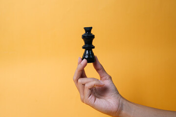 Hand holding black chess piece isolated on yellow background	