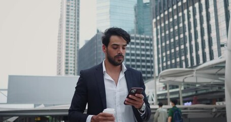 Entrepreneur walks along street, finishing coffee and holding phone. Man takes sip of aromatic drink and glances down street, examining buildings. Energetic gait reflects rhythm life business street.