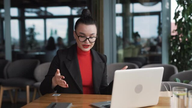 beautiful, stern young woman in business attire argues and gestures with her hands during a video call on a laptop, sitting in an office