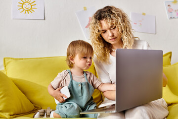 A curly-haired mother and her toddler daughter sit on a couch, engrossed in a laptop screen.