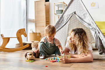 A curly-haired mother and her toddler daughter engage in imaginative play with educational toys,...