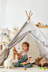 A little girl sits in awe in front of a teepee tent, her eyes wide with wonder, ready to embark on...
