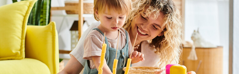 A curly mother and her toddler daughter play together at home using the Montessori method of...