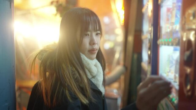 Happy Asian woman choosing and buying drinks on snack and beverage vending machine while shopping at Tokyo city, Japan. Attractive girl enjoy and fun outdoor travel city street on autumn vacation.