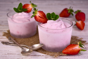 Strawberry ice cream in glasses on a white wooden background.
