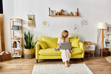 Curly toddler girl on yellow couch, absorbed in using laptop at home.