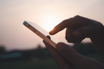 Close up of man hand using smartphone in the dark, against illuminated light sunset