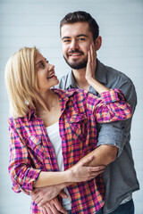 Portrait of young cheerful loving couple smiling looking at camera and hugging each other on light background