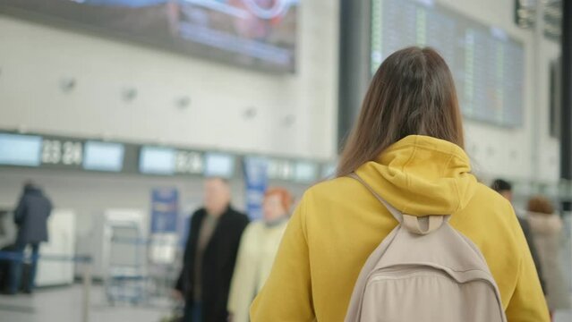 A person wearing a yellow hoodie is observing airport flight information boards