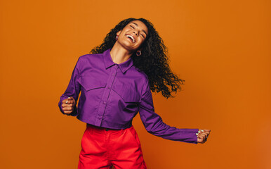 Vibrant woman dancing in casual clothing in a colourful studio with orange background