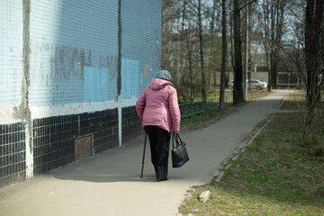Pensioner in the city. Woman with walking stick outdoors. A man goes on the road.
