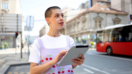 Beautiful, young short-haired woman using a digital tablet on the street