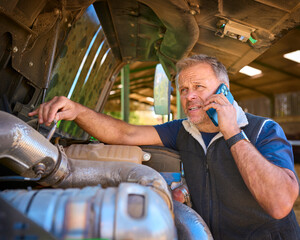 Close Up Of Mature Male Farm Worker On Phone Trying To Fix Machinery