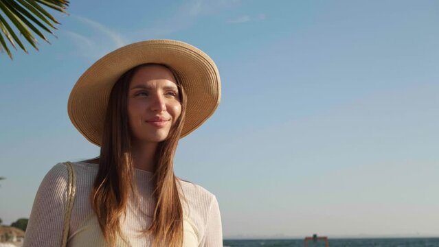 Beautiful woman in hat walking on beach in morning,  low angle view. Camera moving backwards