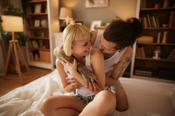 Tattooed man and beautiful woman embracing at home in bed