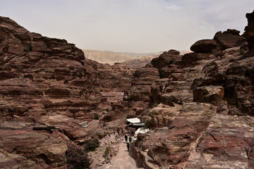 Ausblick von der Wanderung des Klosters von Ad Deir nahe der Felsenstadt von Petra in Jordanien, während sich der Wanderweg durch eine Felsschlucht führt und Touristen auf diesem laufen.