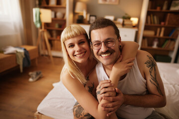 Tattooed man and beautiful woman embracing at home in bed