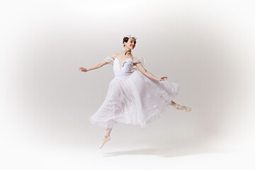 Fototapeta premium Charming ballerina in classic white dress, tutu showcasing her exquisite pose on stage against white studio background. Concept of art, fusion of classic and modernity, grace and elegance.