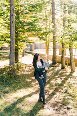 Mom looks at a little girl in her arms walking in a sunny autumn park