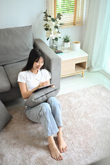 Happy young woman using digital tablet sitting carpet in living room