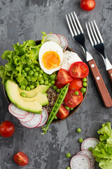 Bowl with healthy salad of quinoa, avocado, legumes, herbs, cherry tomatoes, egg and cream cheese on a dark background. View from above. The concept of proper nutrition, self-care and health.