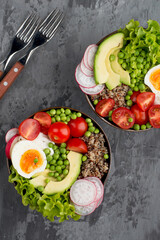 Bowl with healthy salad of quinoa, herbs, vegetables with cutlery on a dark background. View from above. The concept of proper nutrition, self-care and health.