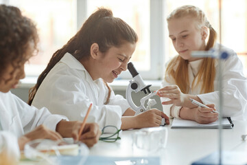 Selective focus shot of Middle Eastern girl wearing lab coat sitting at table in classroom looking...