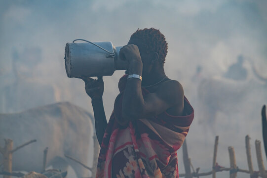 Backlight photo of a man in a Mundari cattle camp drinking milk, Mundari tribe, South Sudan