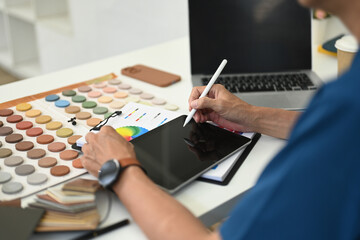 Cropped shot male interior designer using digital tablet at working desk with color swatch samples