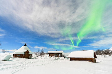 Typical wooden buildings covered with snow under the Northern Lights (Aurora Borealis), full moon night, Kilpisjarvi, Enontekio municipality, Finnish Lapland, Finland, Scandinavia