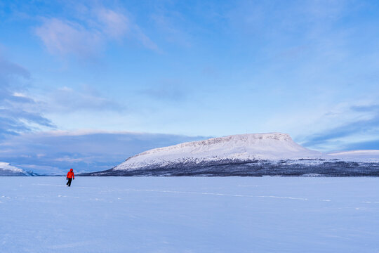 Man in the Arctic landscape walks on the icy surface of a Finnish lake in front of Saana hill (fell) at dusk, Kilpisjarvi, Enontekio municipality, Finnish Lapland, Finland, Scandinavia