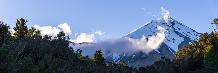 Panoramic view of Mount Taraniki, snowy volcano summit with a blue sky and forest in the evening, North Island, New Zealand, Pacific