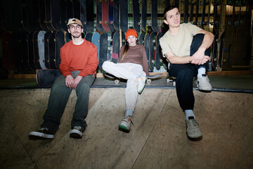 Group of self-confident young men and woman sitting relaxed in skatepark having rest after skateboarding practice