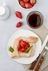Puff pastry with strawberries, coffee with milk on a light background, top view.