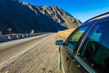 Black motor vehicle on the side of the asphalt road, with majestic mountains in the background.