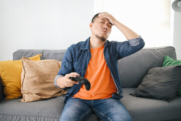Young Man Holds Joystick, Touching Forehead Showing Disappointed Expression Because Loss The Game...