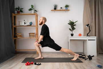 Athletic man doing forward lunge exercises at home in his apartment with cozy Interior.