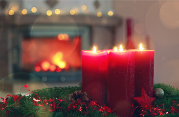 Four burning red Advent candles in a warm interior with fireplace.