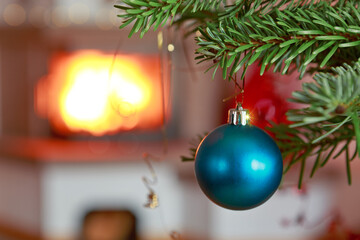 Christmas ball on fir tree branch and blur burning fireplace background.
