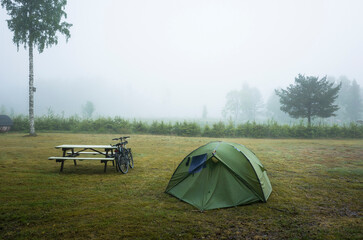 Green tent on camping ground, Two bicycles stand next to a wooden table on a foggy day, Eco tourism...