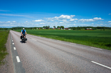 Cyclist on touring bicycle solo travel in Värmland, Sweden, Nordic countryside, Road among fields...
