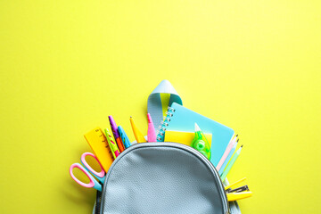 Back to school concept with vibrant school supplies spilling from a backpack on a yellow background