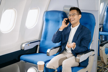 Attractive Asian male passenger of airplane sitting in comfortable seat while working laptop and tablet with mock up area using wireless connection.