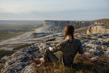 Woman sitting on cliff edge admiring majestic valley and mountains with travel and adventure concept