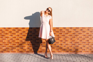 Happy beautiful young woman with a smile with vintage sunglasses in a pink summer dress with a bag...