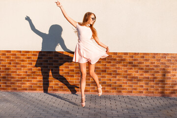 Beautiful positive young fashionable woman in a fashion pink dress jumping and having fun near the...