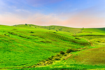 Fototapeta premium scenic view of beautiful rural landscape with green hills and fields with young grass and amazing cloudy sky on background