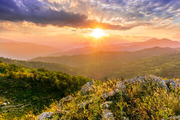 highland mountain landscape of beautiful sunset or sunrise with nice mountain peaks and slopes, green and golden hills and majestic cloudy sky on background