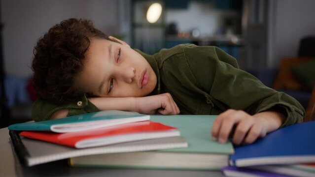 African American multiethnic sad upset tired exhausted fatigued overworked stressed boring little boy son kid child schoolboy pupil at home education lying on books at table relax sleepy studying